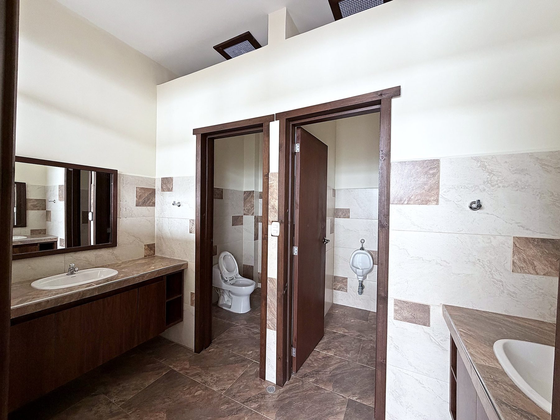 Baños con mesón de lavamanos, espejo y dos puertas de madera hacia los sanitarios