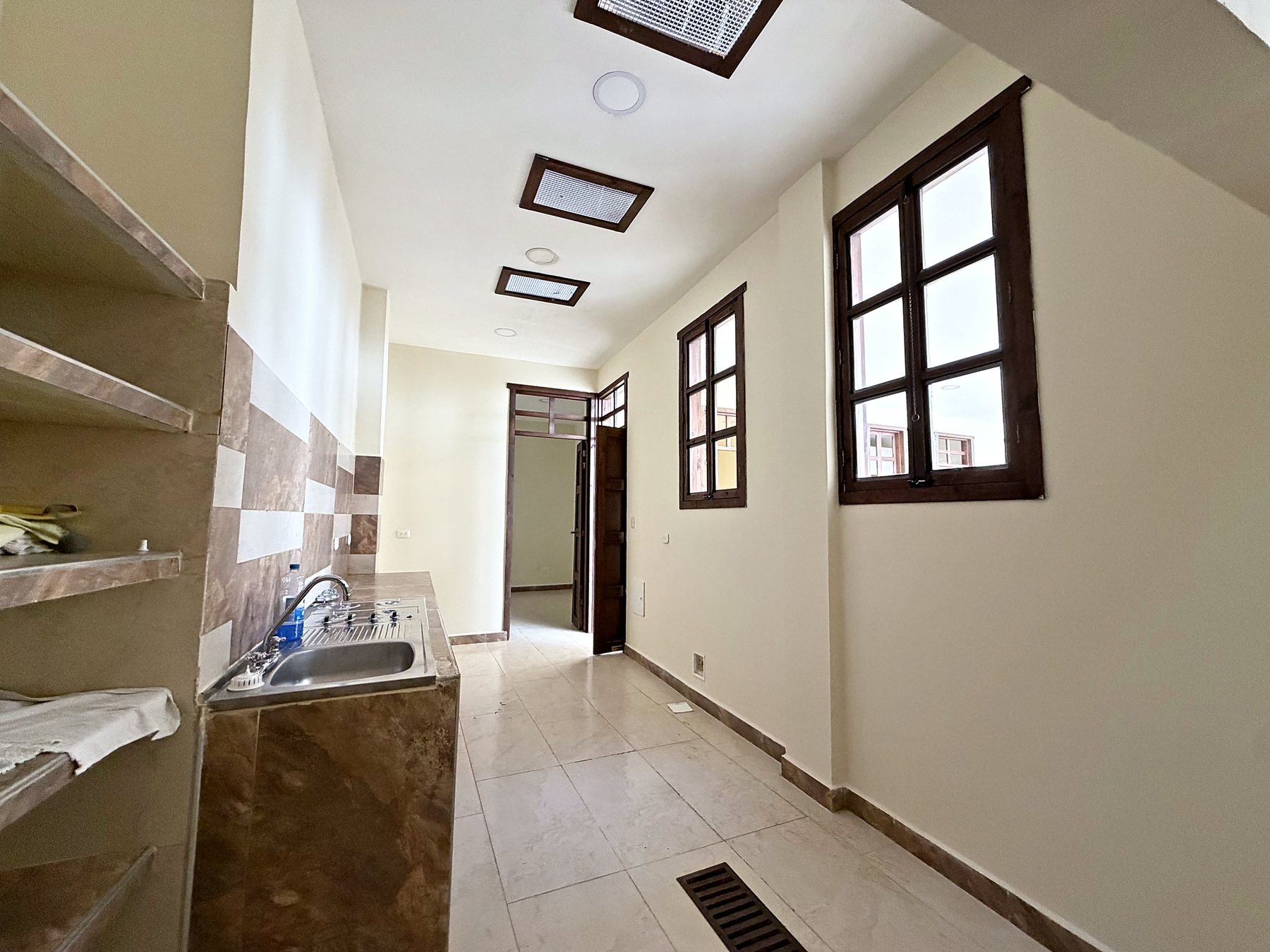 Cocina con mesón y lavaplatos, estanterías y pasillo con ventanas de madera