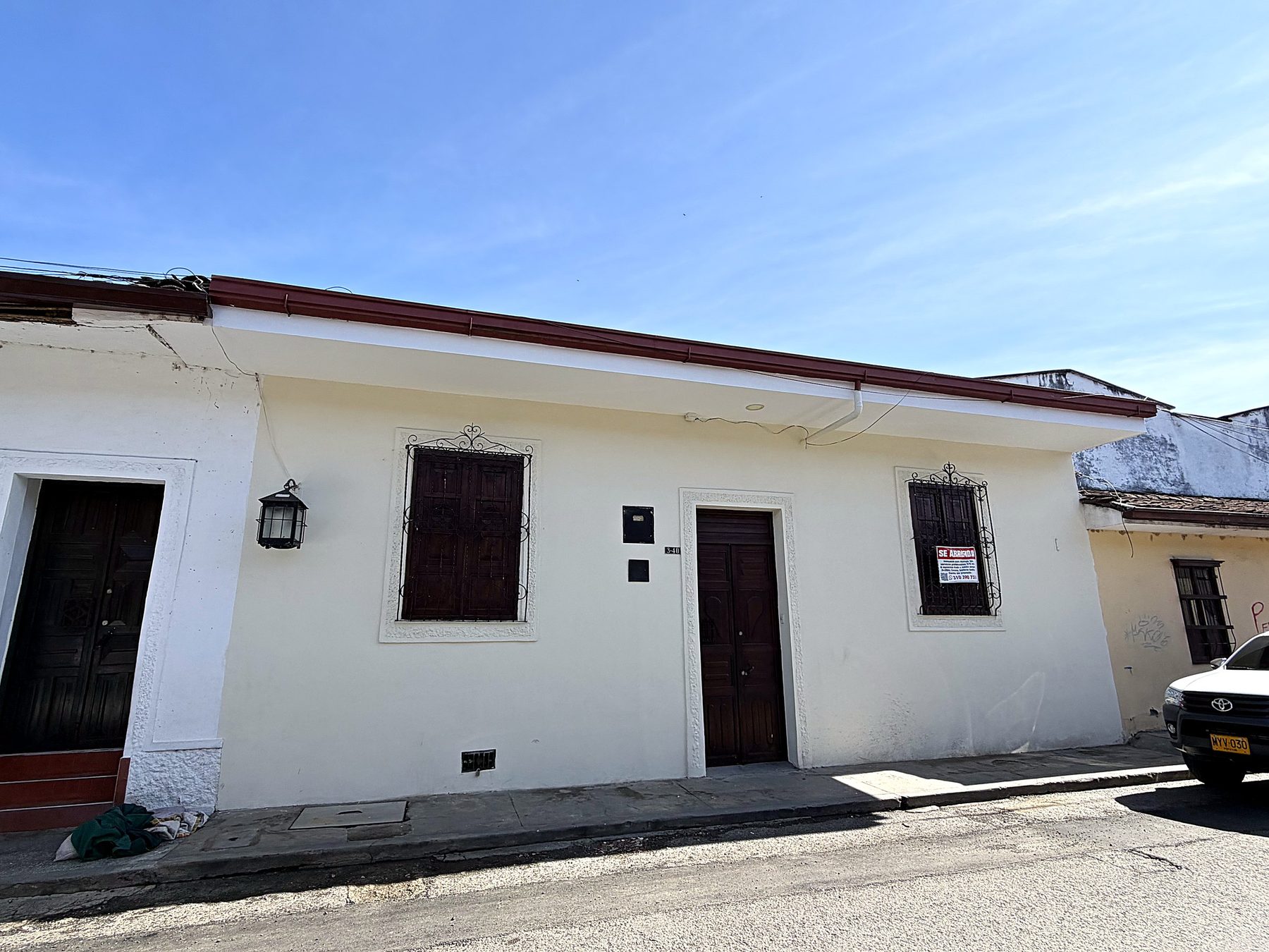 Fachada blanca de la casona con puertas y ventanas de madera, faroles y rejas de forja