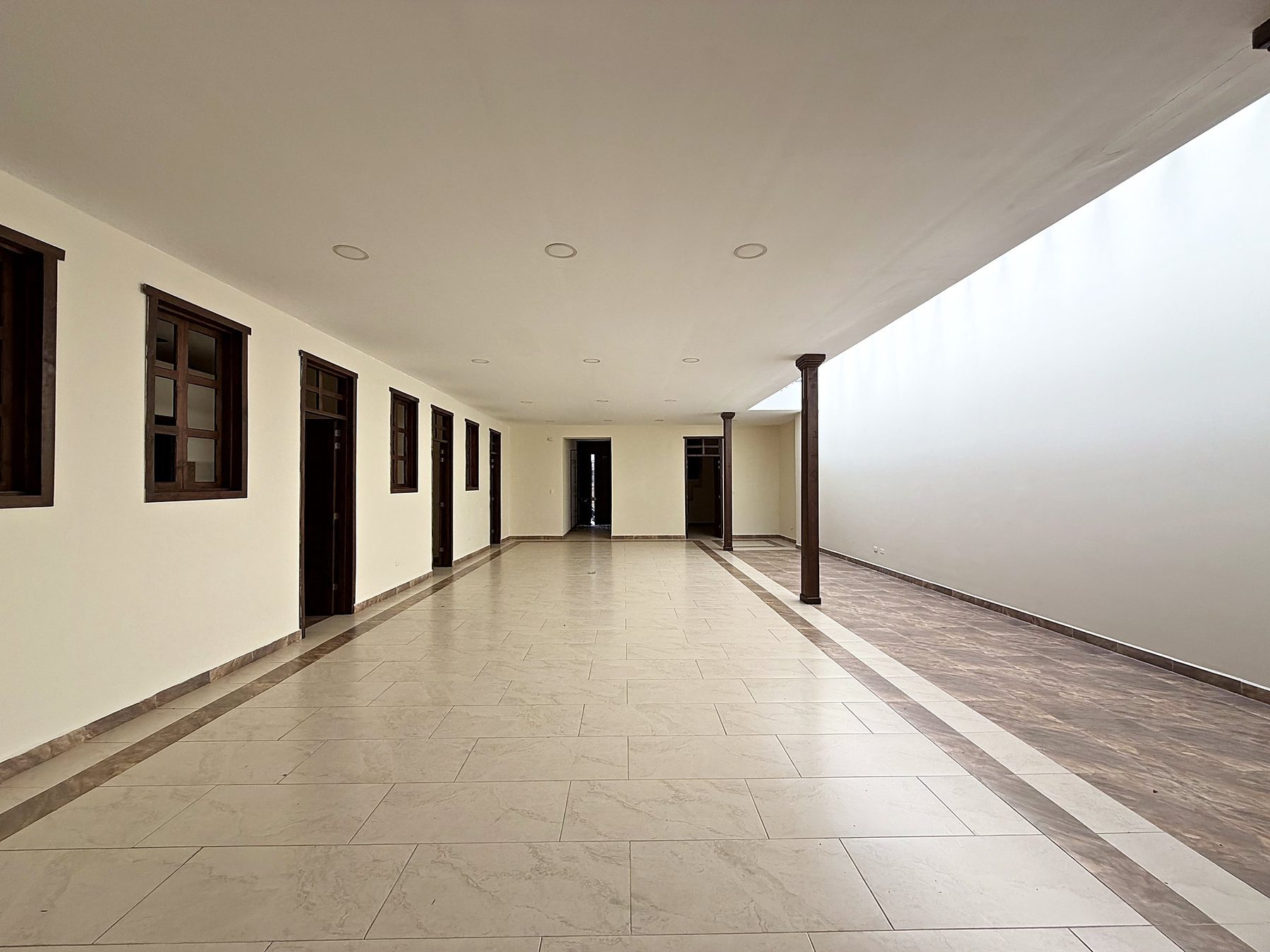 Salón central de 8 por 20 metros con pisos claros, columna de madera y puertas de las oficinas a un costado