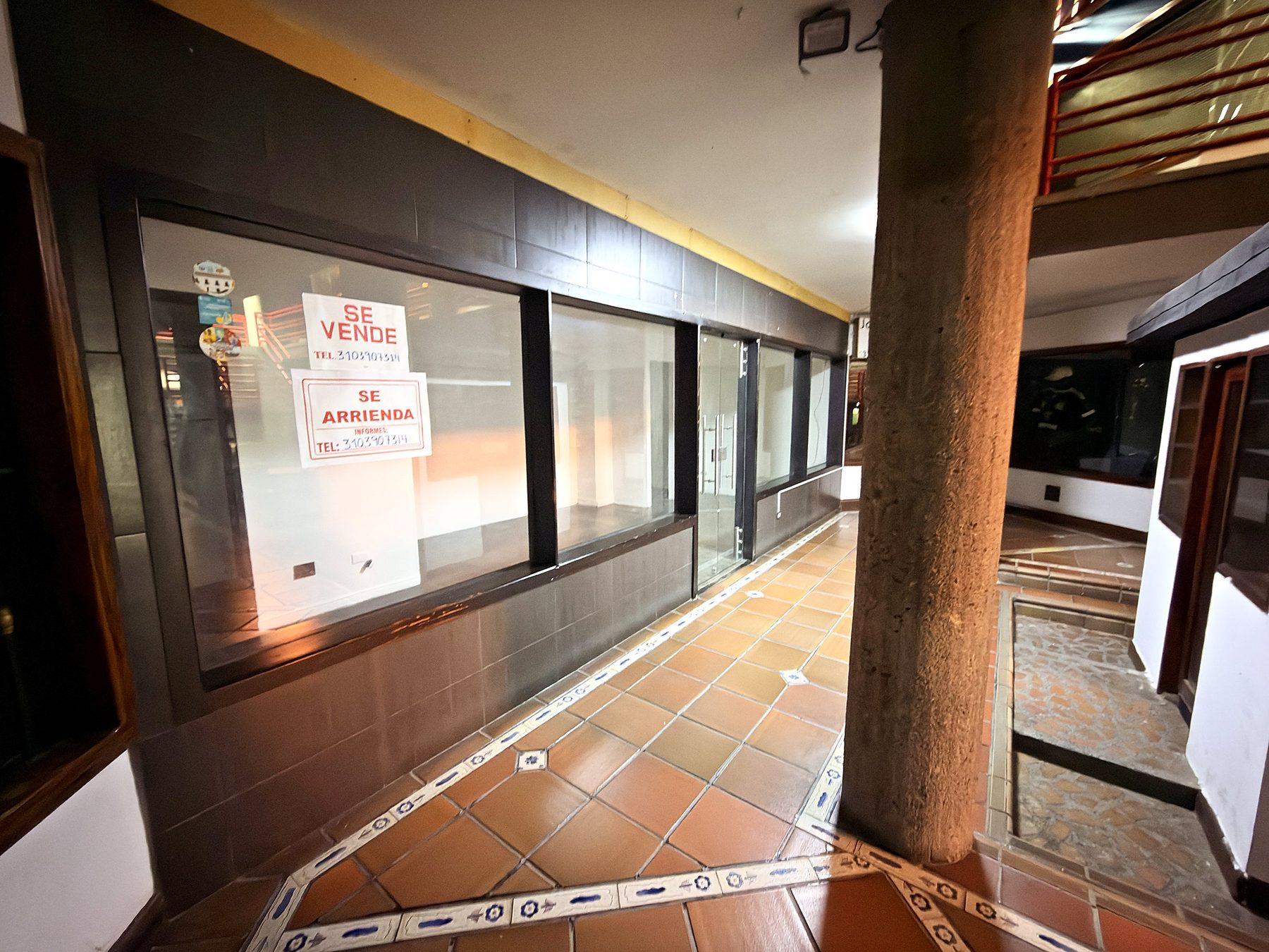 Vitrina del local sobre el pasillo del centro comercial, con avisos de venta y arriendo
